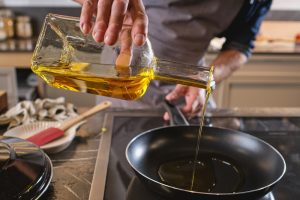 Unrecognizable man pouring oil into frying pan